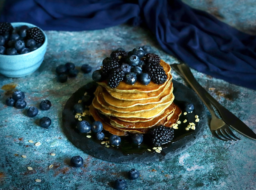 a stack of pancakes with blueberries and blackberries on a plate