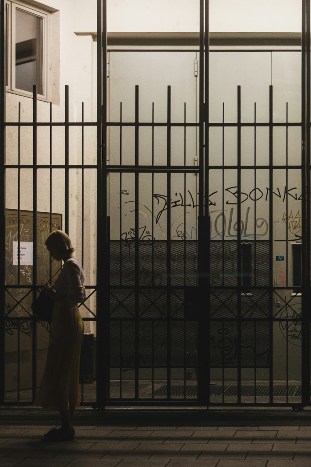 a woman standing in front of a gate with graffiti on it