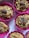 An arrangement of baked muffins topped with almonds, set in bright pink silicone baking cups. The muffins appear to have a grainy texture with visible oats and seeds.
