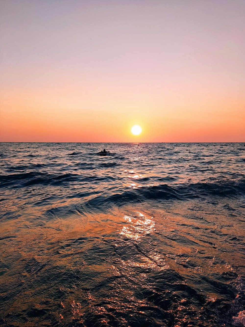 the sun is setting over the ocean with a boat in the distance