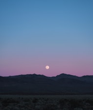the moon is setting over a mountain range
