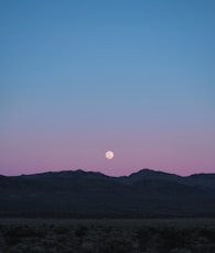 the moon is setting over a mountain range