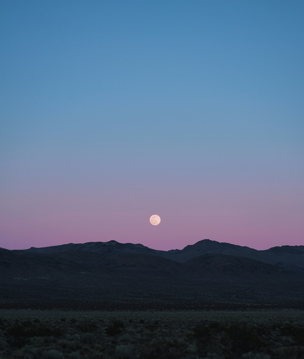 the moon is setting over a mountain range