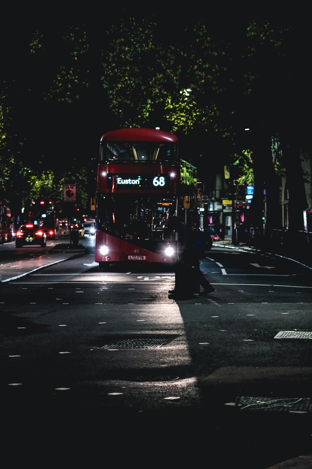 a red double decker bus driving down a street at night