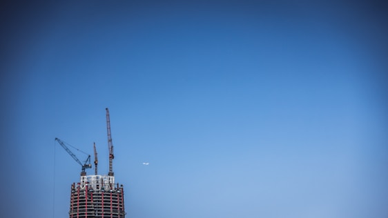A construction site with workers collaborating under a clear blue sky, showcasing cranes and building frameworks.