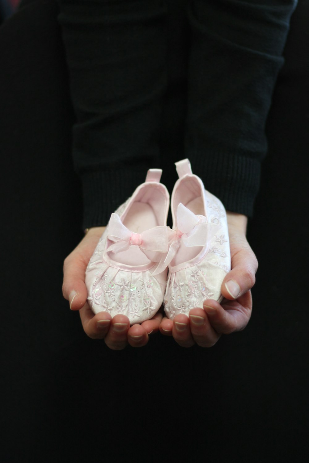 a person holding a pair of white baby shoes