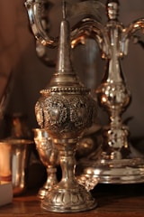Intricate silver goblets and ornate metalware with detailed engravings and a reflective surface are displayed. The objects have a rich patina, suggesting age and craftsmanship.