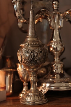 Intricate silver goblets and ornate metalware with detailed engravings and a reflective surface are displayed. The objects have a rich patina, suggesting age and craftsmanship.