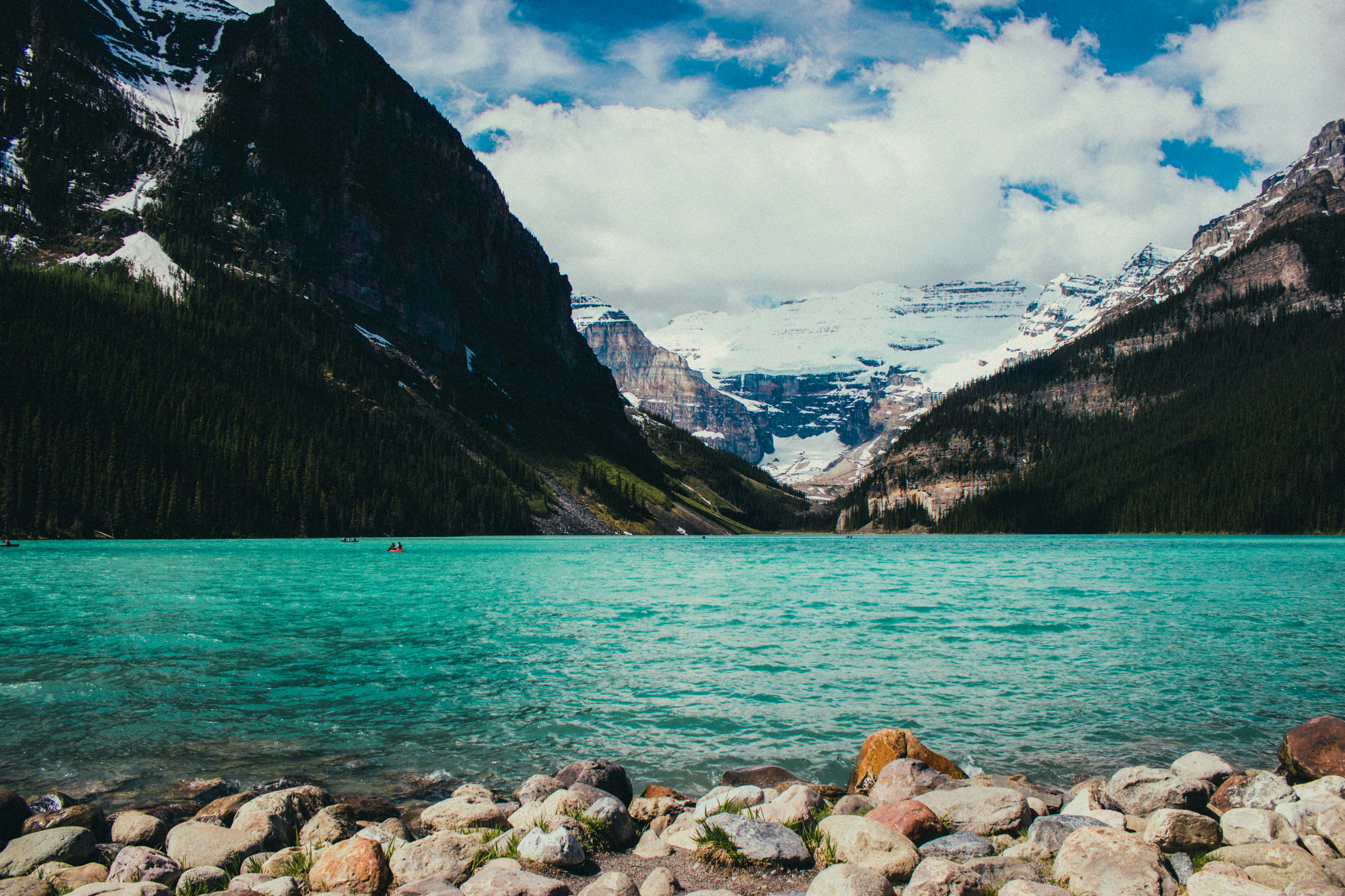 A rocky beach next to a body of water with Lake Louise in the background  photo – Free Mountains Image on Unsplash, image size:3000x2000