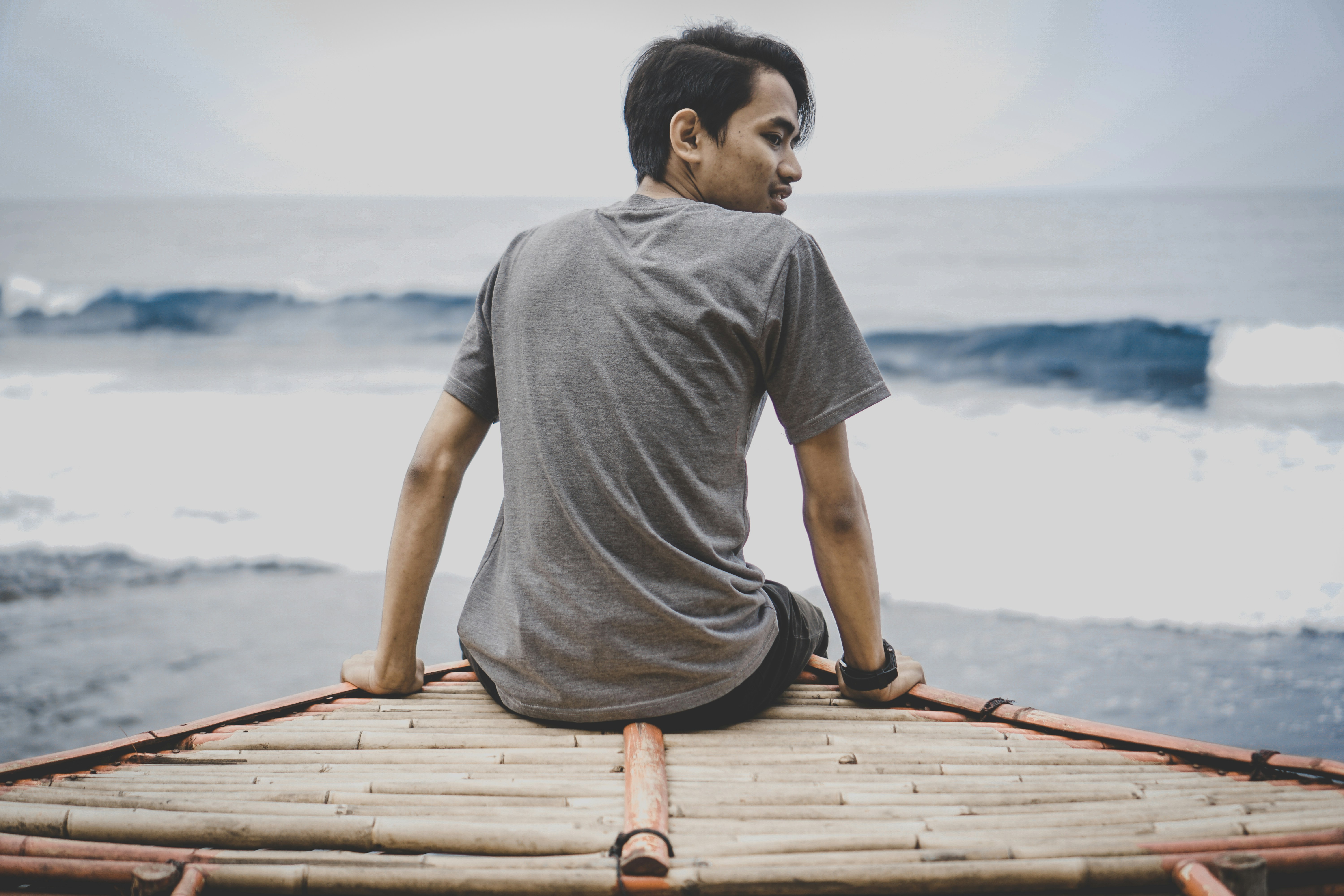 a man sitting on top of a bamboo raft near the ocean - Yogyakarta
