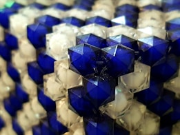 Close-up of hexagonal blue and transparent plastic beads arranged in a repetitive pattern. The beads have a faceted surface that reflects light, giving a shiny appearance.