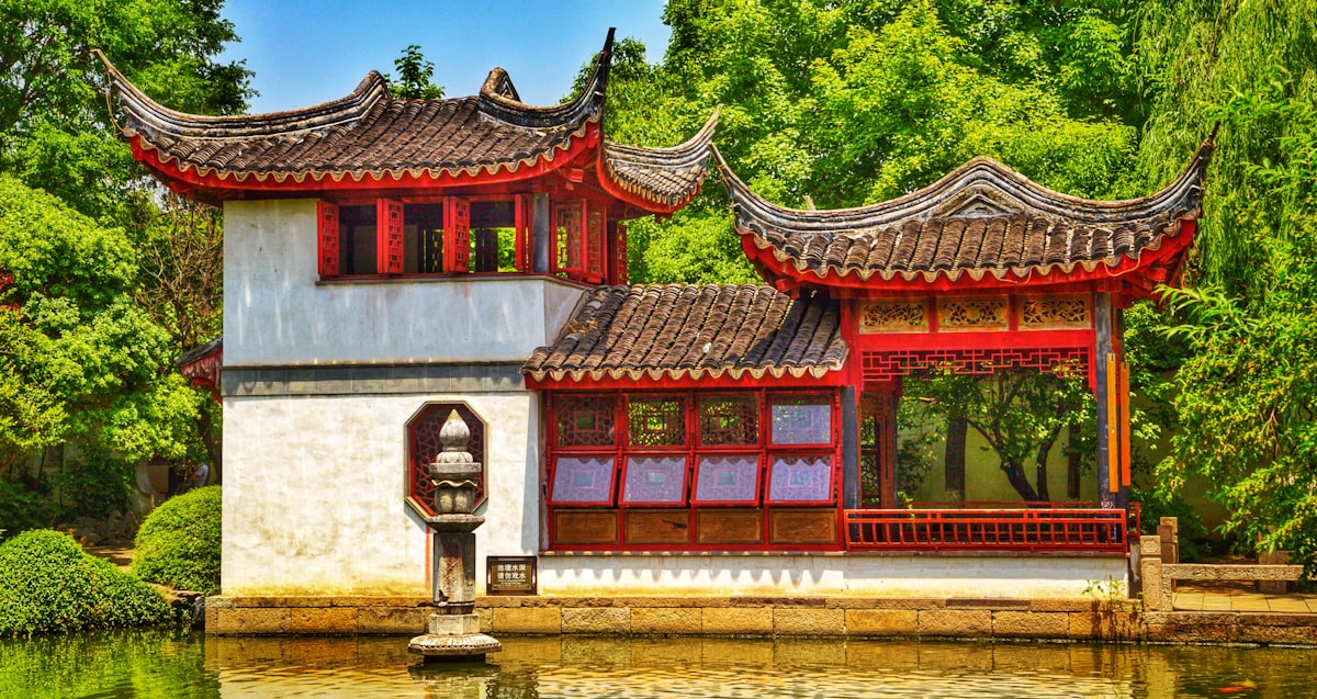 Traditional Chinese pavilion in a Suzhou classical garden with water, bridges, and lush greenery showing the UNESCO World Heritage garden style