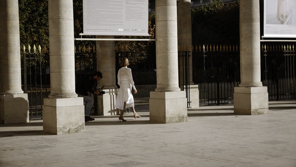 a woman walking down a sidewalk next to tall pillars