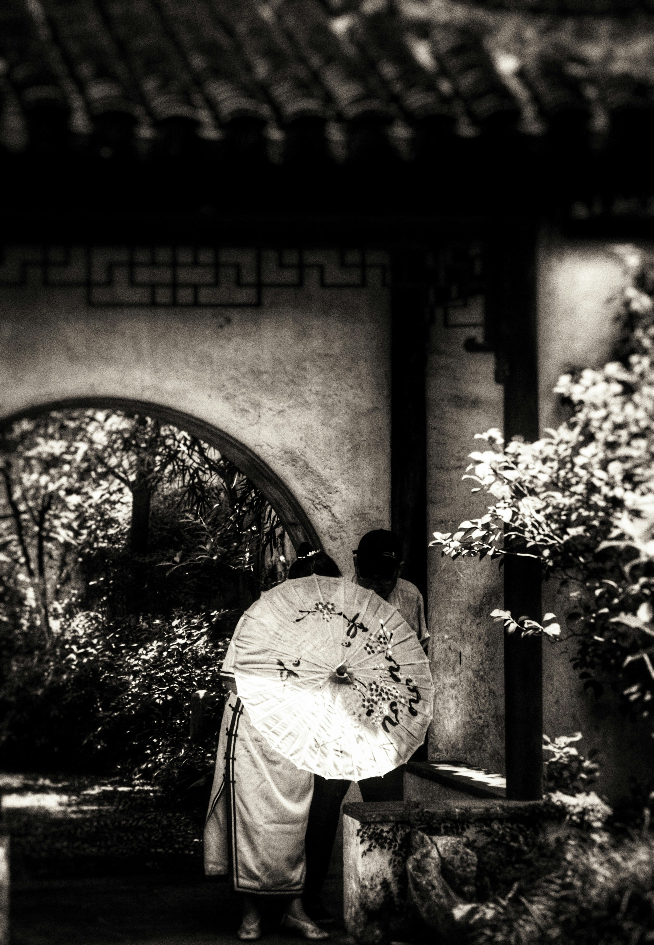 Old Chinese couple with a traditional sunshade in a Chinese garden in Suzhou, China
