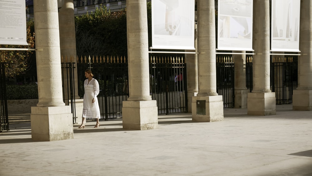 a woman walking down a sidewalk next to tall pillars