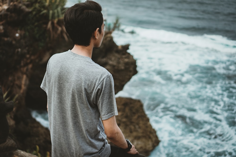 a man sitting on a rock looking at the ocean