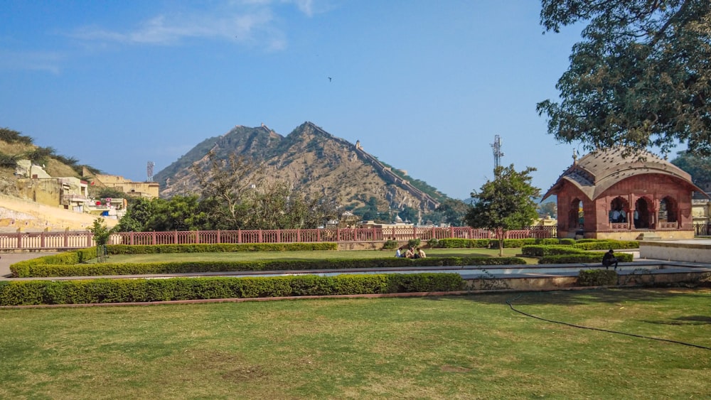 a grassy area with a fountain and mountains in the background