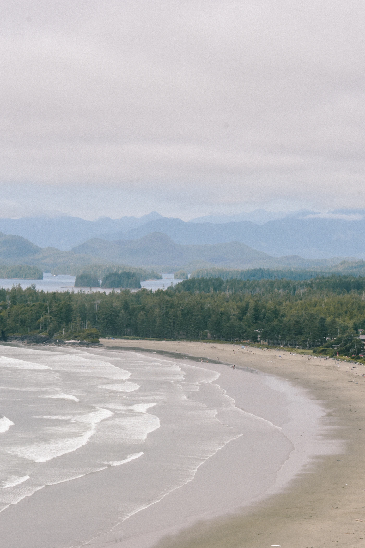 Wide empty beach at Tofino, BC with forested mountains in the background