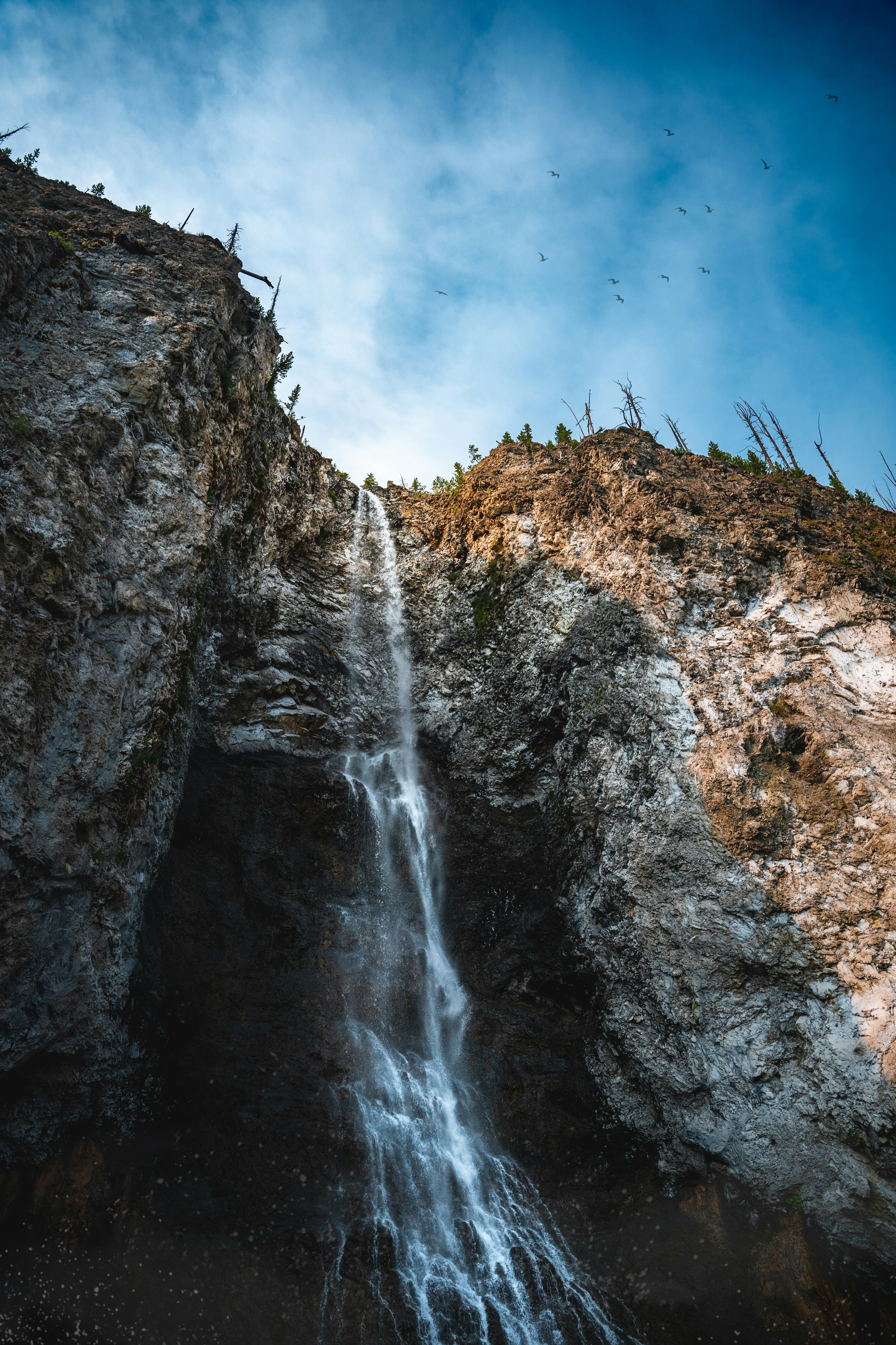 a very tall waterfall with a bunch of birds flying over it