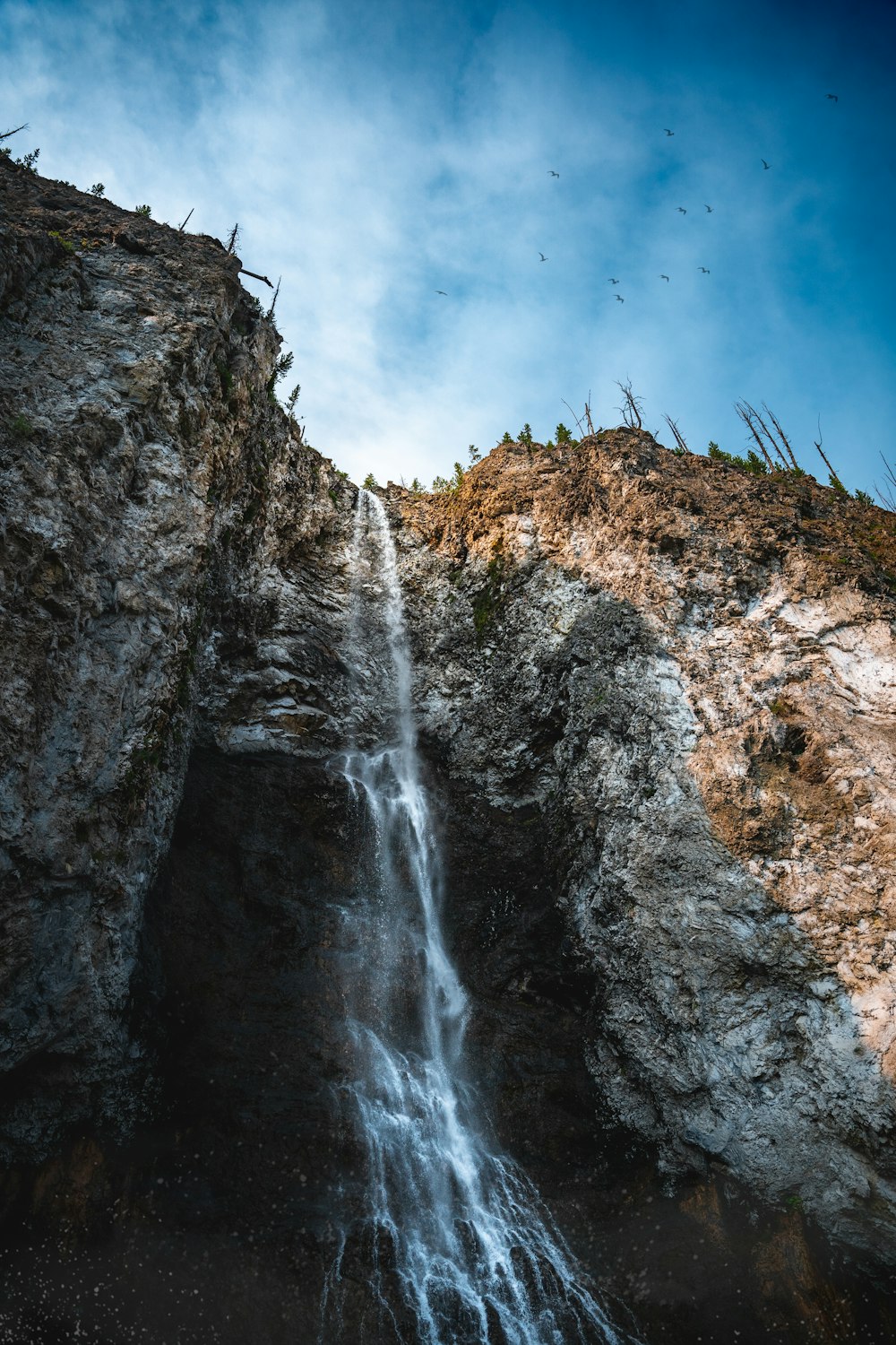 a very tall waterfall with a bunch of birds flying over it