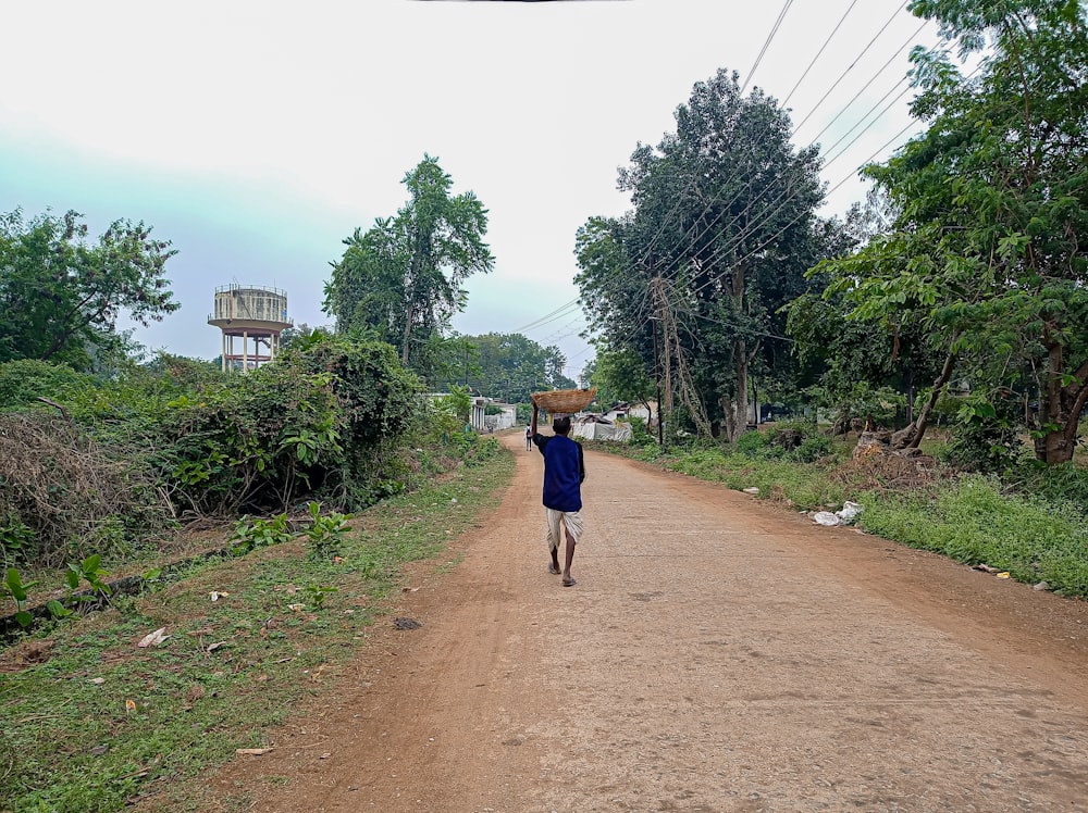 a man walking down a dirt road carrying a basket on his head