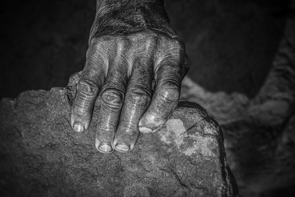 a black and white photo of a person's hand resting on a rock