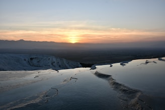 the sun is setting over a snowy mountain