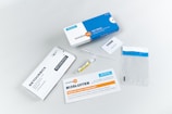 A collection of items related to a test kit, including a white and blue box labeled 'testalize.me', a sealed return envelope, a small vial, an information booklet, a code card, a pipette, and a clear plastic bag with a blue strip.