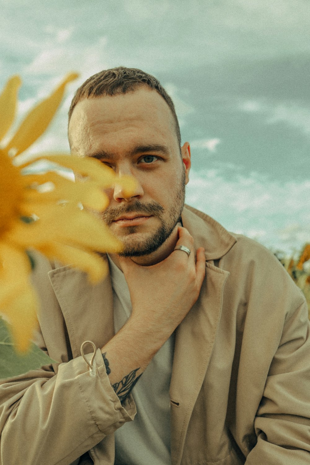 a man in a trench coat standing next to a sunflower