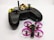 A black remote control with dual joysticks is positioned beside a small quadcopter drone. The drone features vivid pink propeller guards and has a compact, lightweight design, indicating it might be designed for indoor or recreational use. A keychain with a golden key and a black and orange lanyard is attached to the remote.