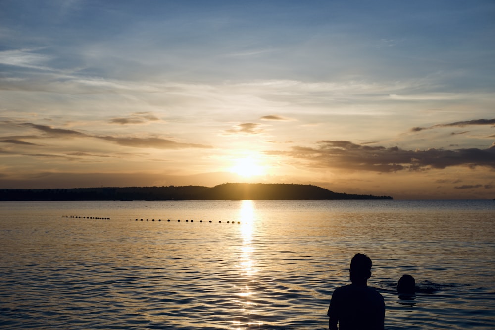 a person standing in the water watching the sun set