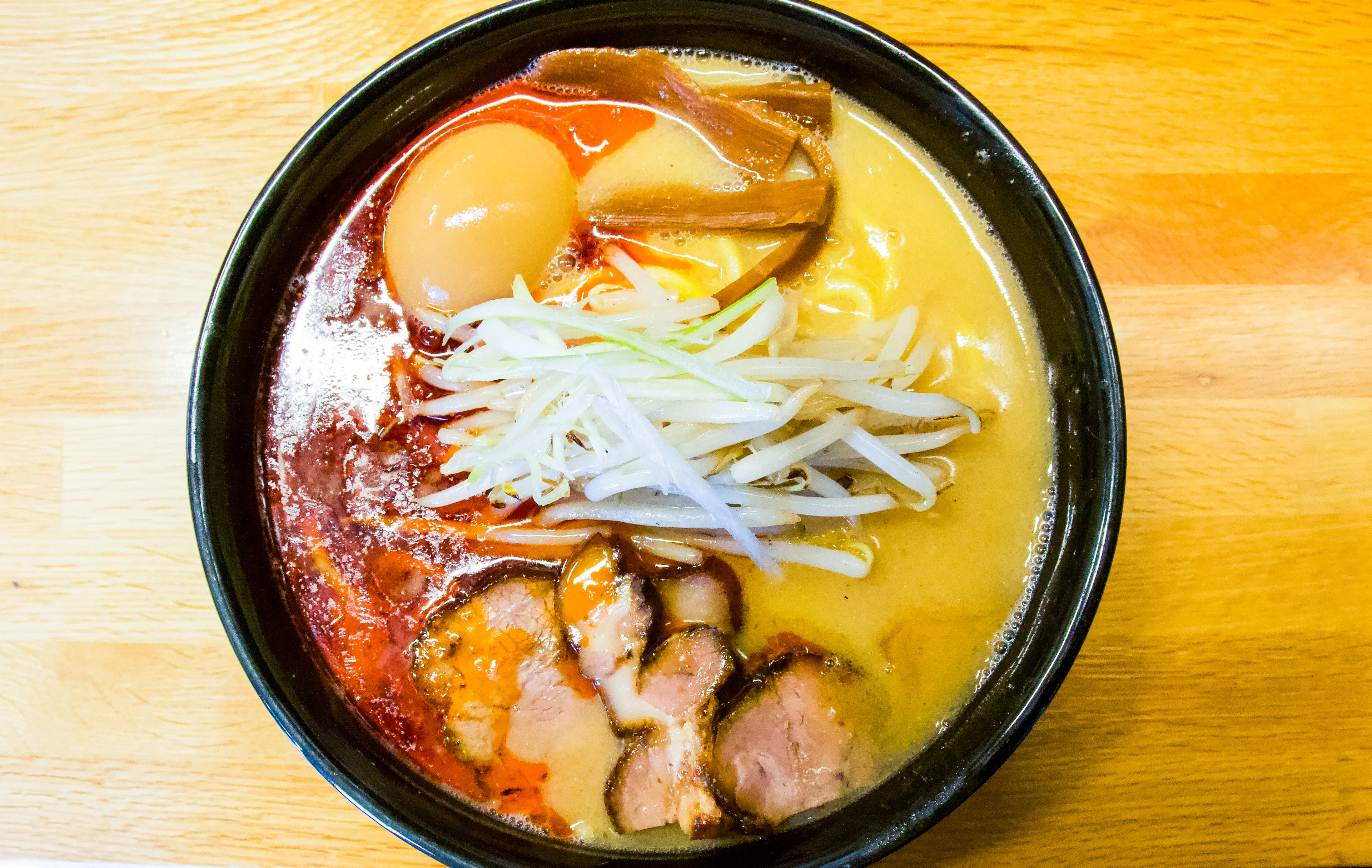 A bowl of spicy miso ramen with slices of chashu pork, bean sprouts, a soft egg and chilli oil in cloudy broth, the miso style of ramen that began in Sapporo