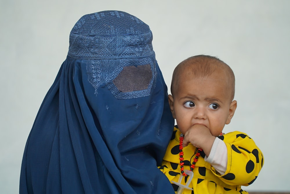 a baby wearing a yellow shirt and a blue head covering