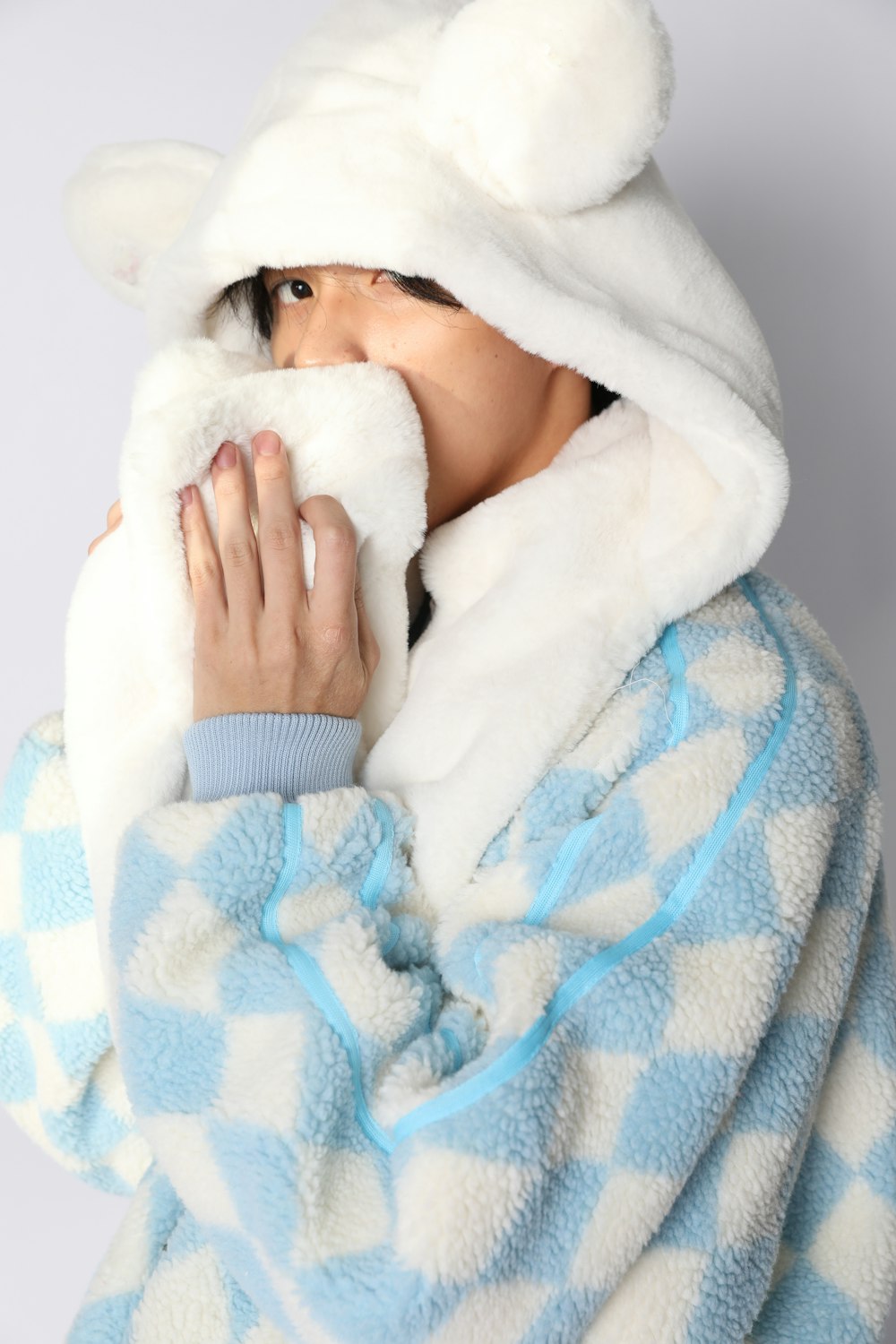 a woman in a blue and white checkered robe covers her face with a white