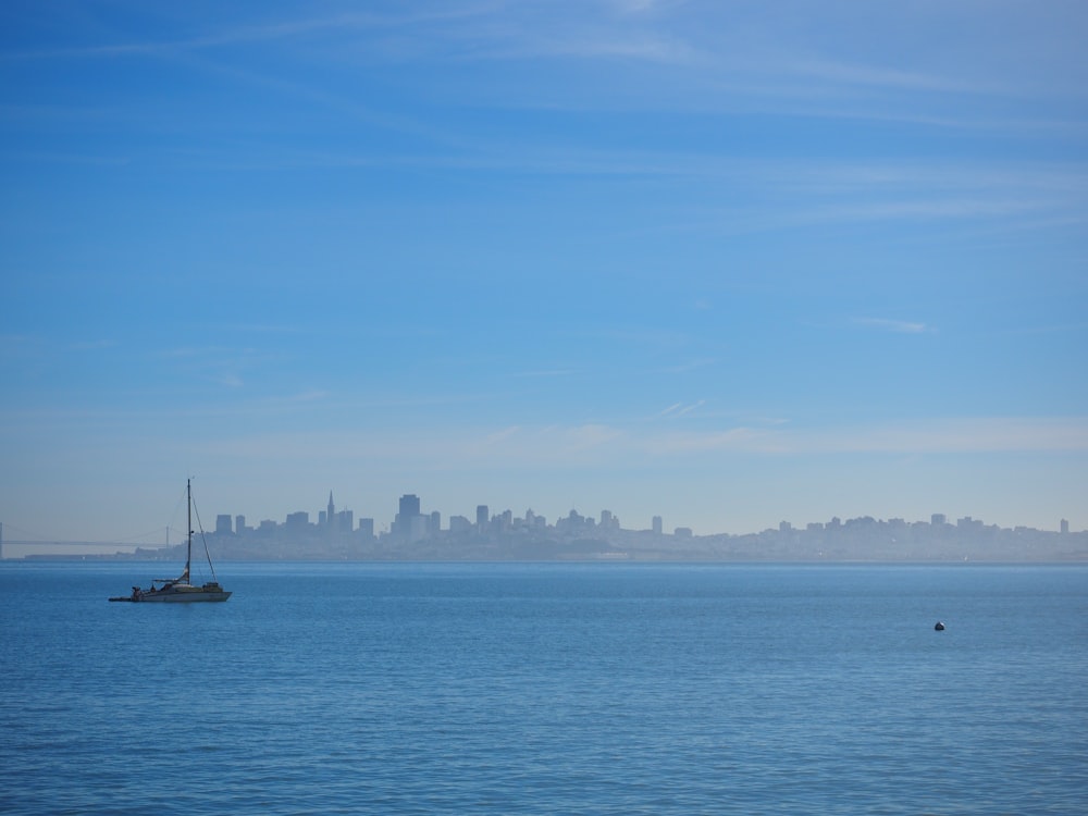 a sailboat in the middle of the ocean with a city in the background