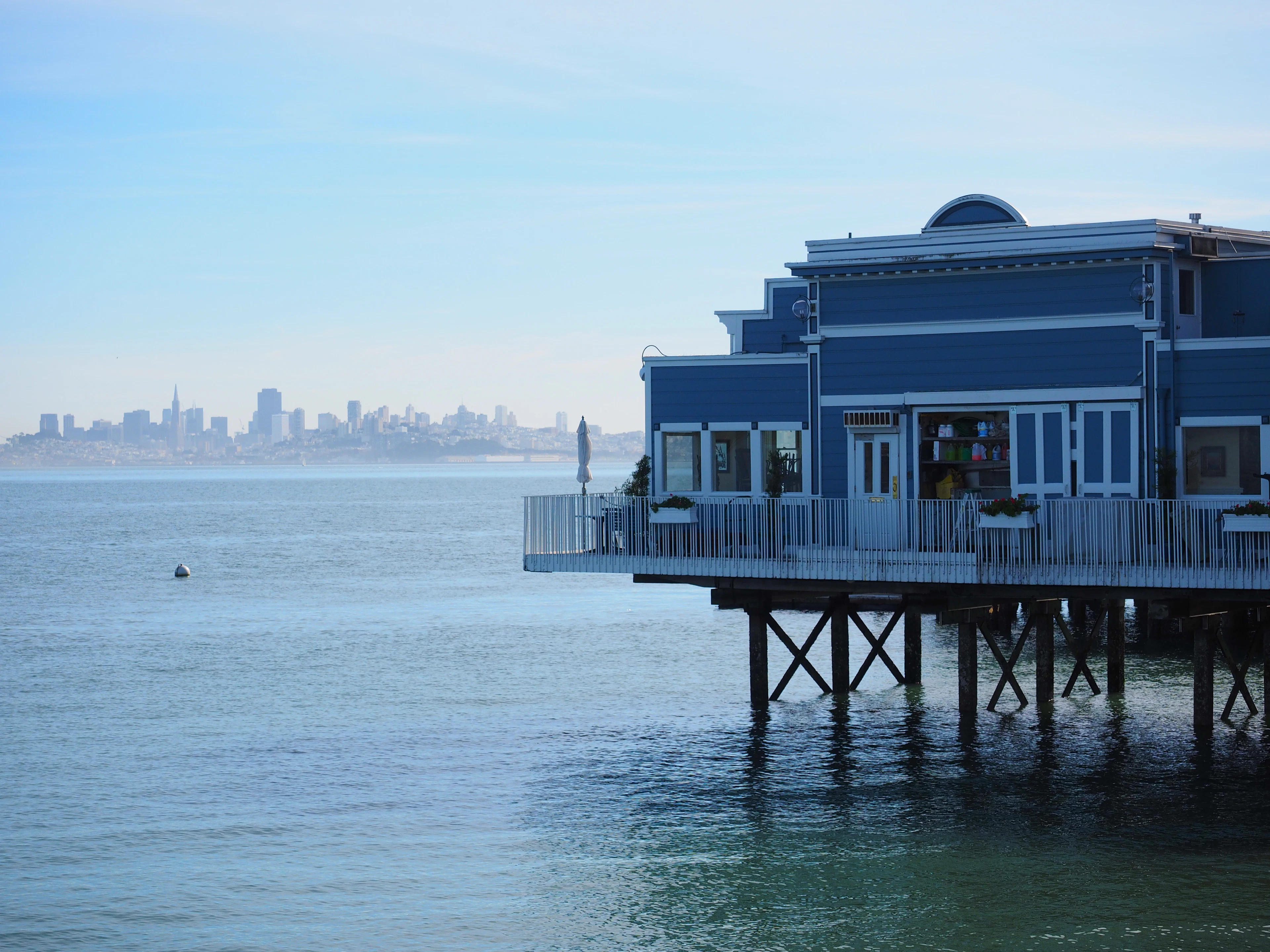 A blue waterfront building in Sausalito with the city across the bay