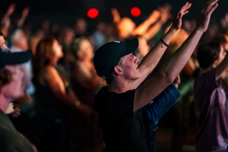 A vibrant gathering of people worshiping together with hands raised in a softly lit church.