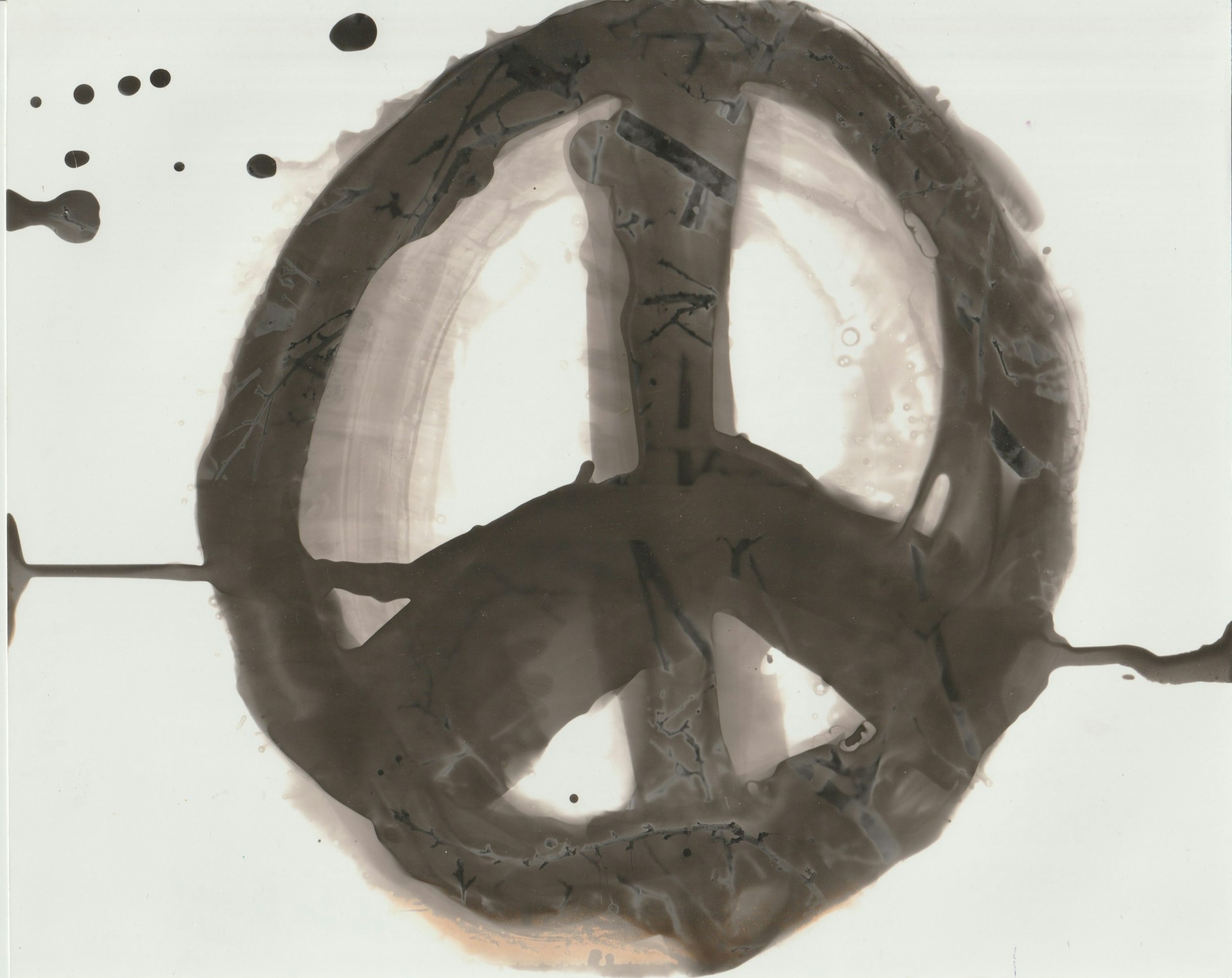 A large peace symbol painted with brush strokes that appear to be in shades of black and gray, set against a white background. The symbol is imperfect and smudged, with splatters and drips surrounding it, adding a raw and expressive quality.