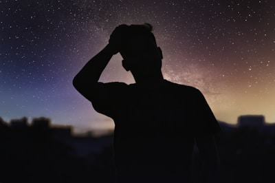 A humanoid AI figure standing contemplatively under a starry sky, with nebulae swirling overhead.