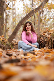 a woman sitting on the ground surrounded by leaves