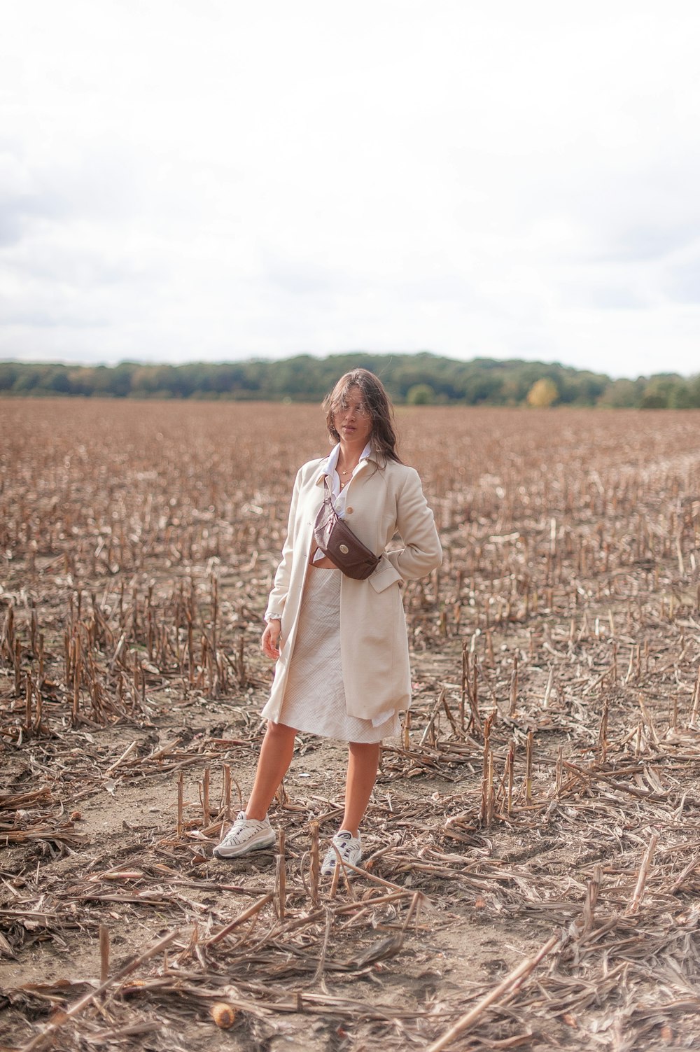 a woman in a trench coat standing in a field