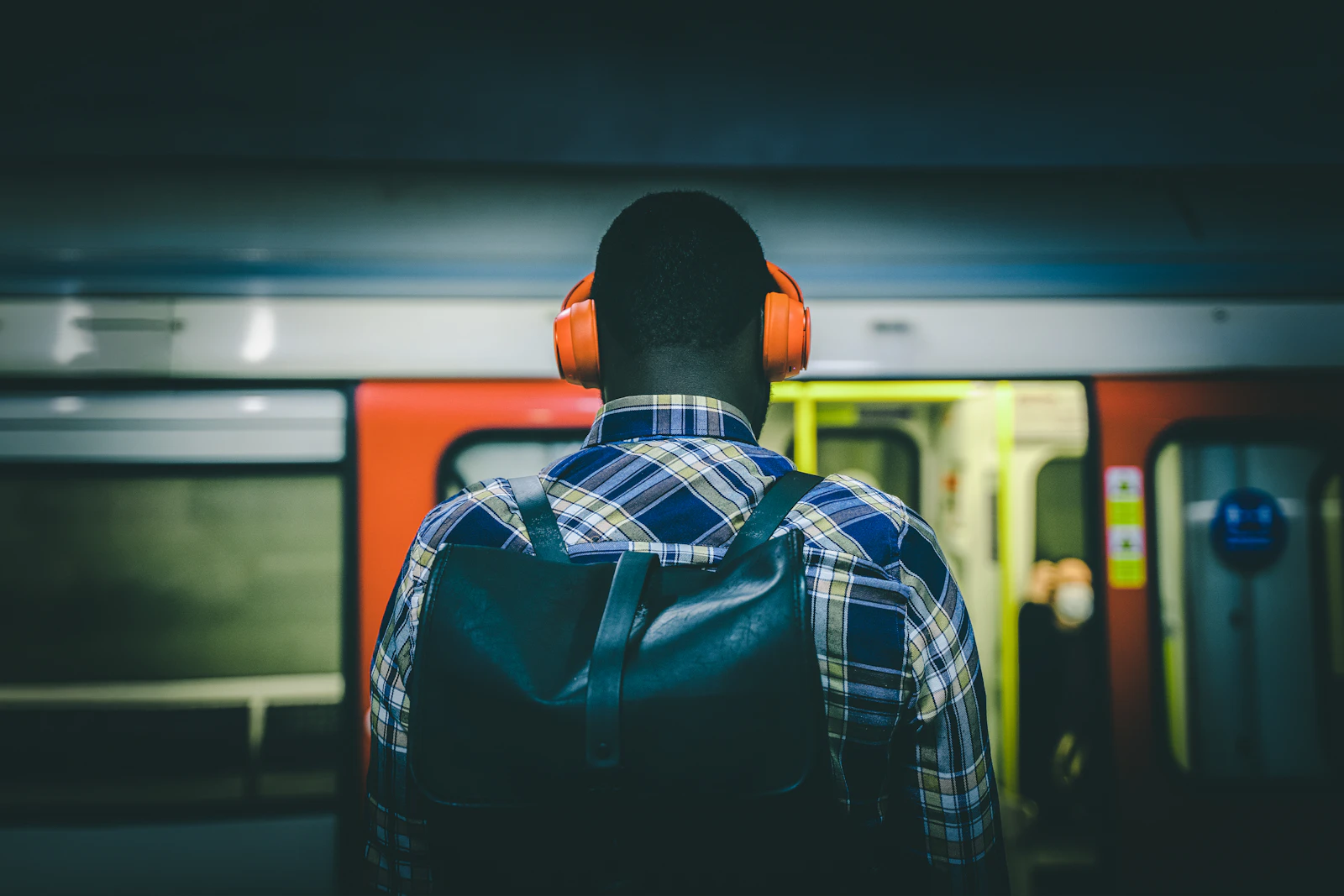 A man wearing headphones standing on a platform as a train passes behind him