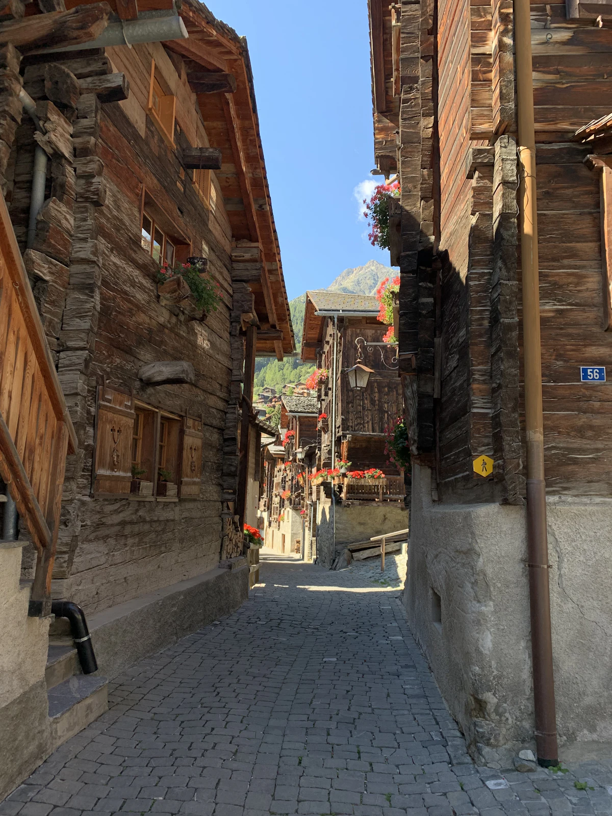 A narrow cobbled lane between old wooden houses with flower boxes in Grimentz