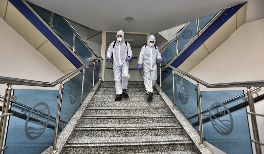two people in white suits walking down a flight of stairs