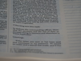 A close-up of a page from a book showing text in two columns. The text appears to be historical or biblical, indicated by the formal language and structure. The page includes a passage discussing a city's rebellious history and the response from a king.