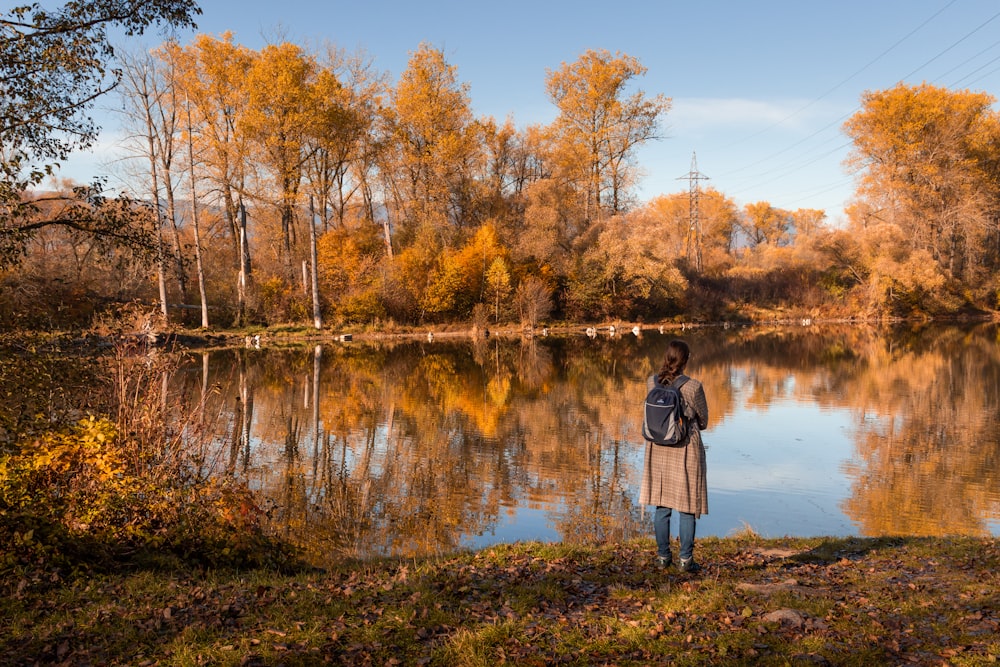 a woman standing in front of a lake surrounded by trees