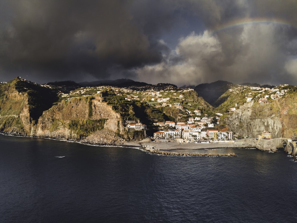 a rainbow is seen over a small town on a cliff