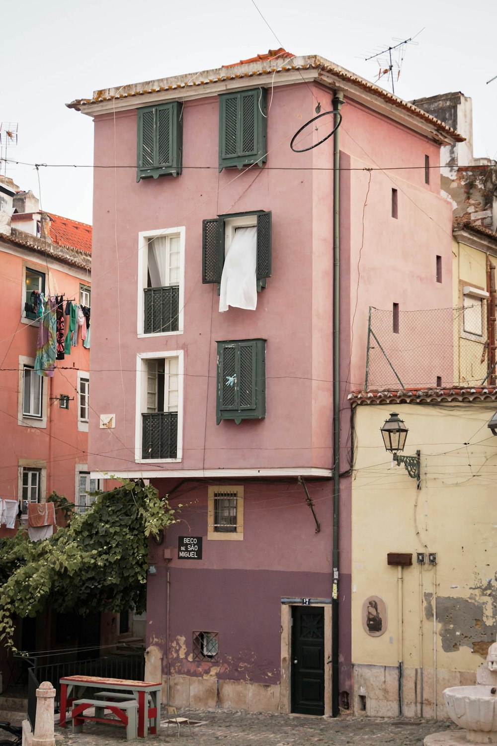 a pink building with green shutters and a red bench