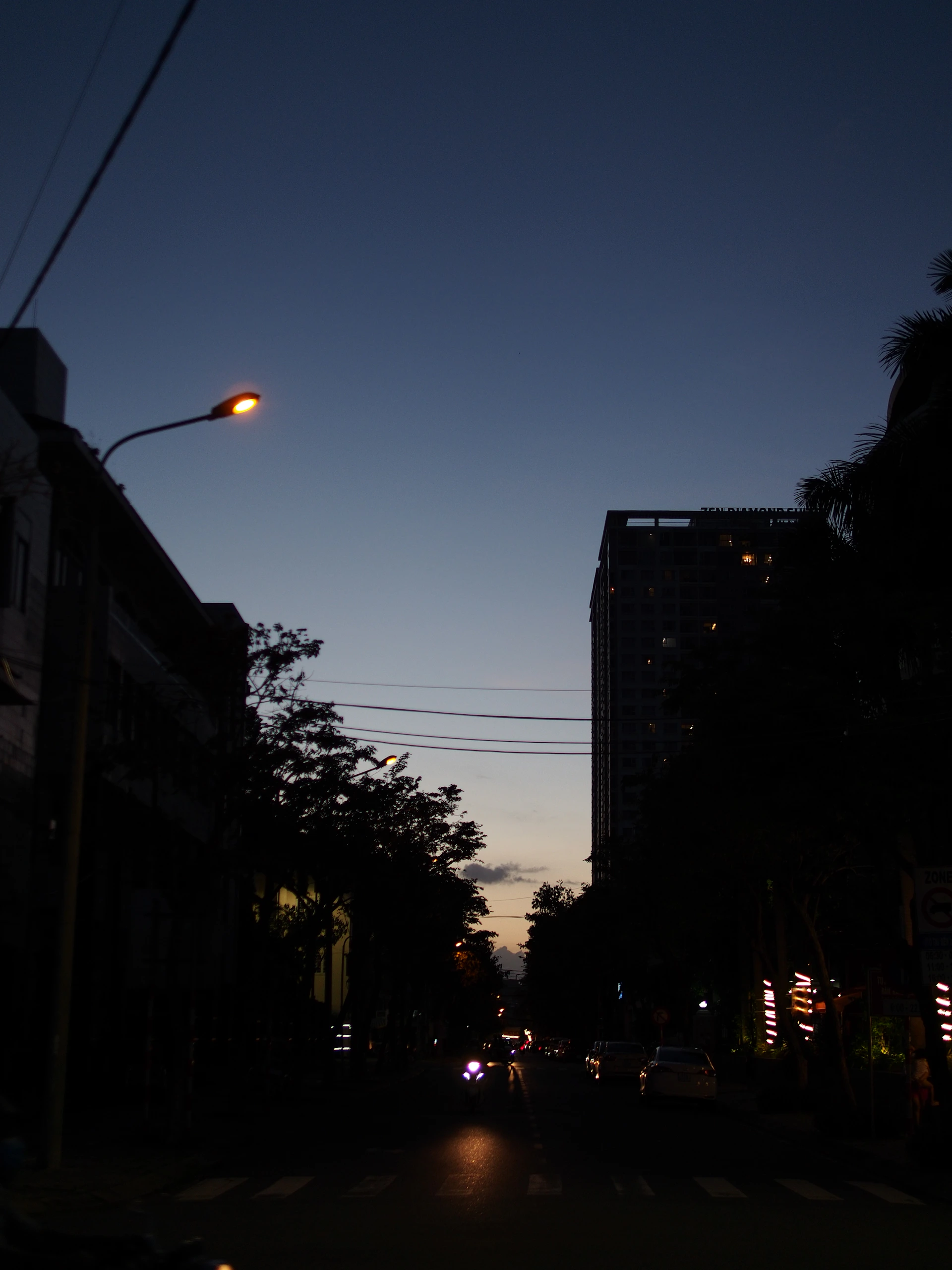 An urban street scene at dusk, with soft lights glowing from windows and subtle shadows on the pavement.