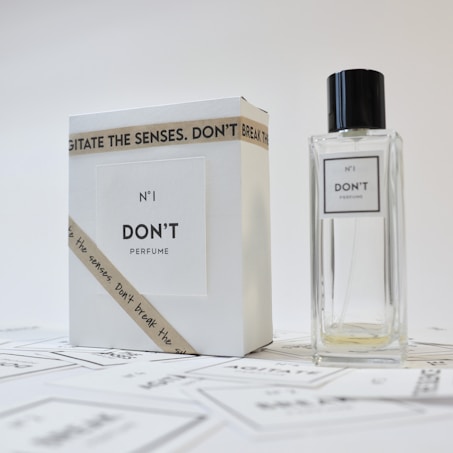 A minimalist design featuring a perfume bottle and its packaging. The bottle is transparent with a simple label, while the box is white with a bold font. A ribbon with the text 'Don't agitate the senses' is wrapped around the box.